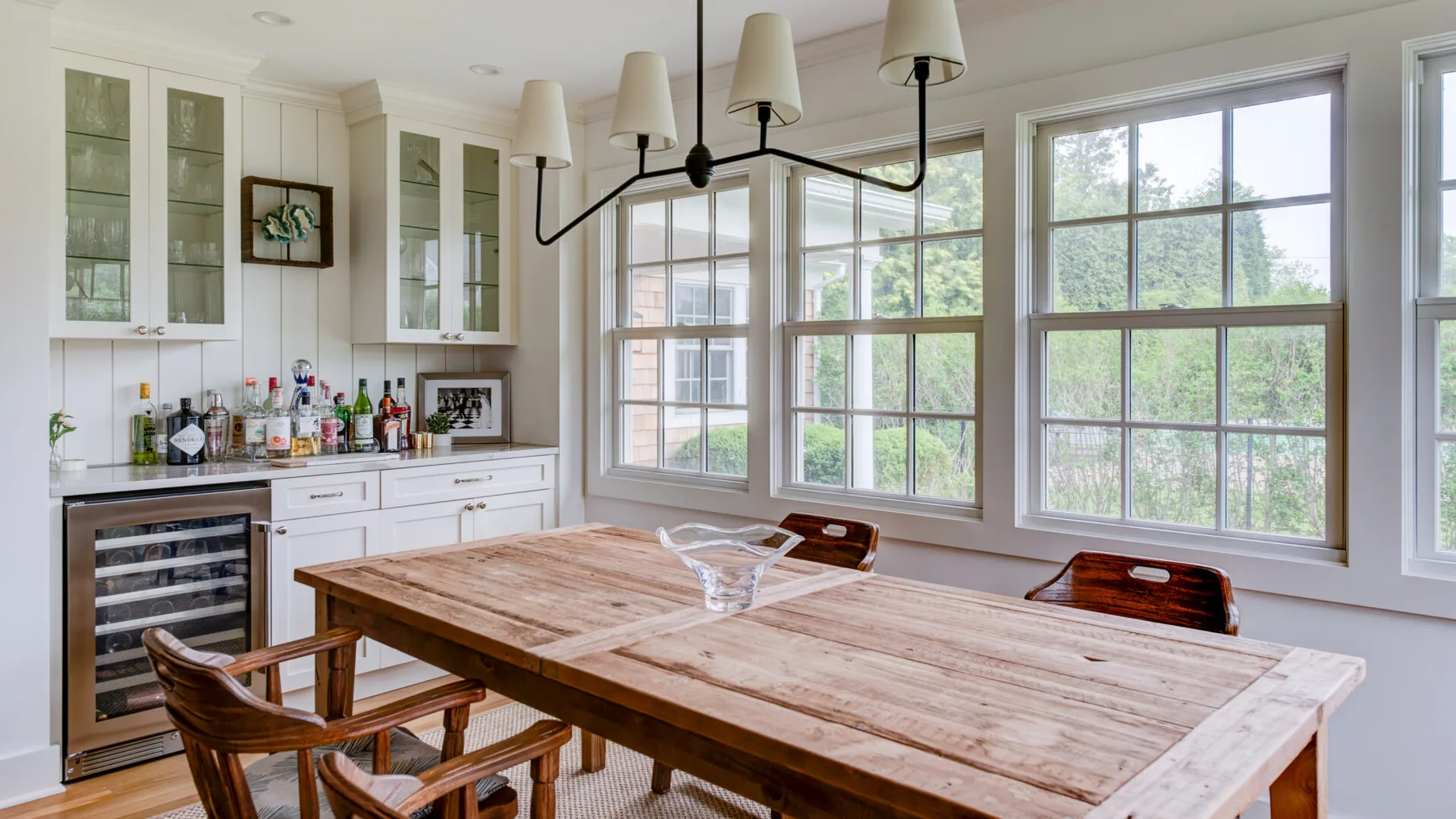 A bright dining area features a wooden table beside large windows.