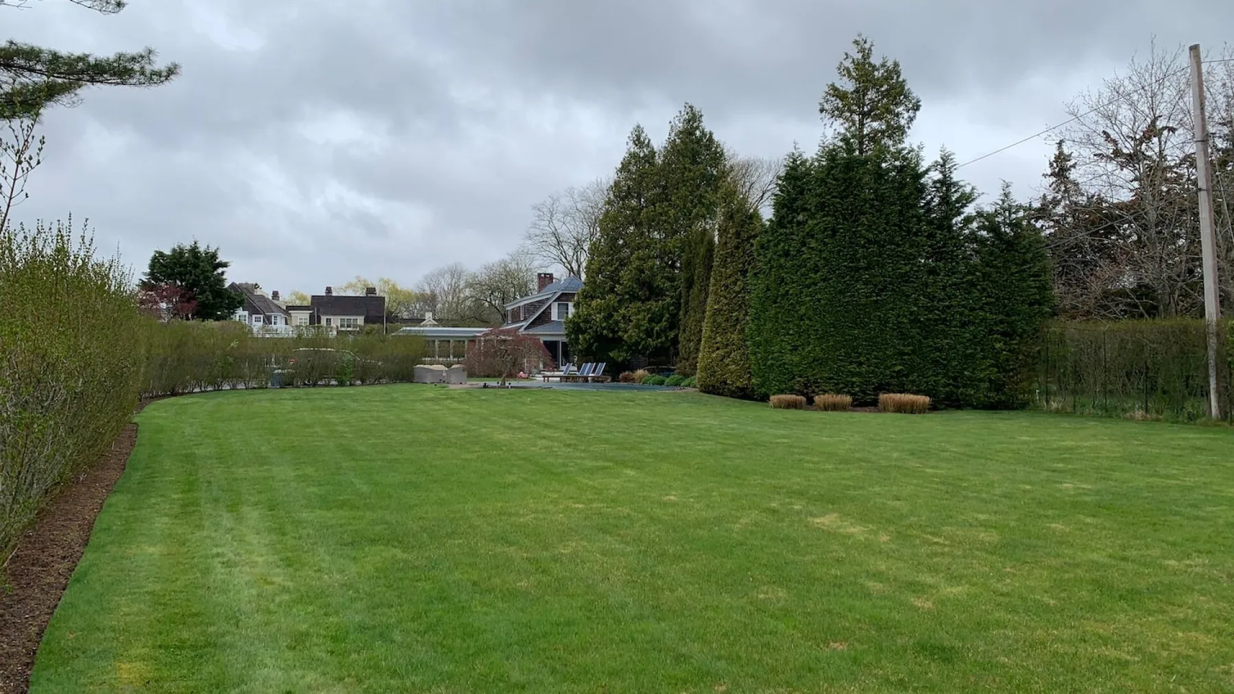 A broad green lawn stretches across a landscaped garden beneath a cloudy sky.