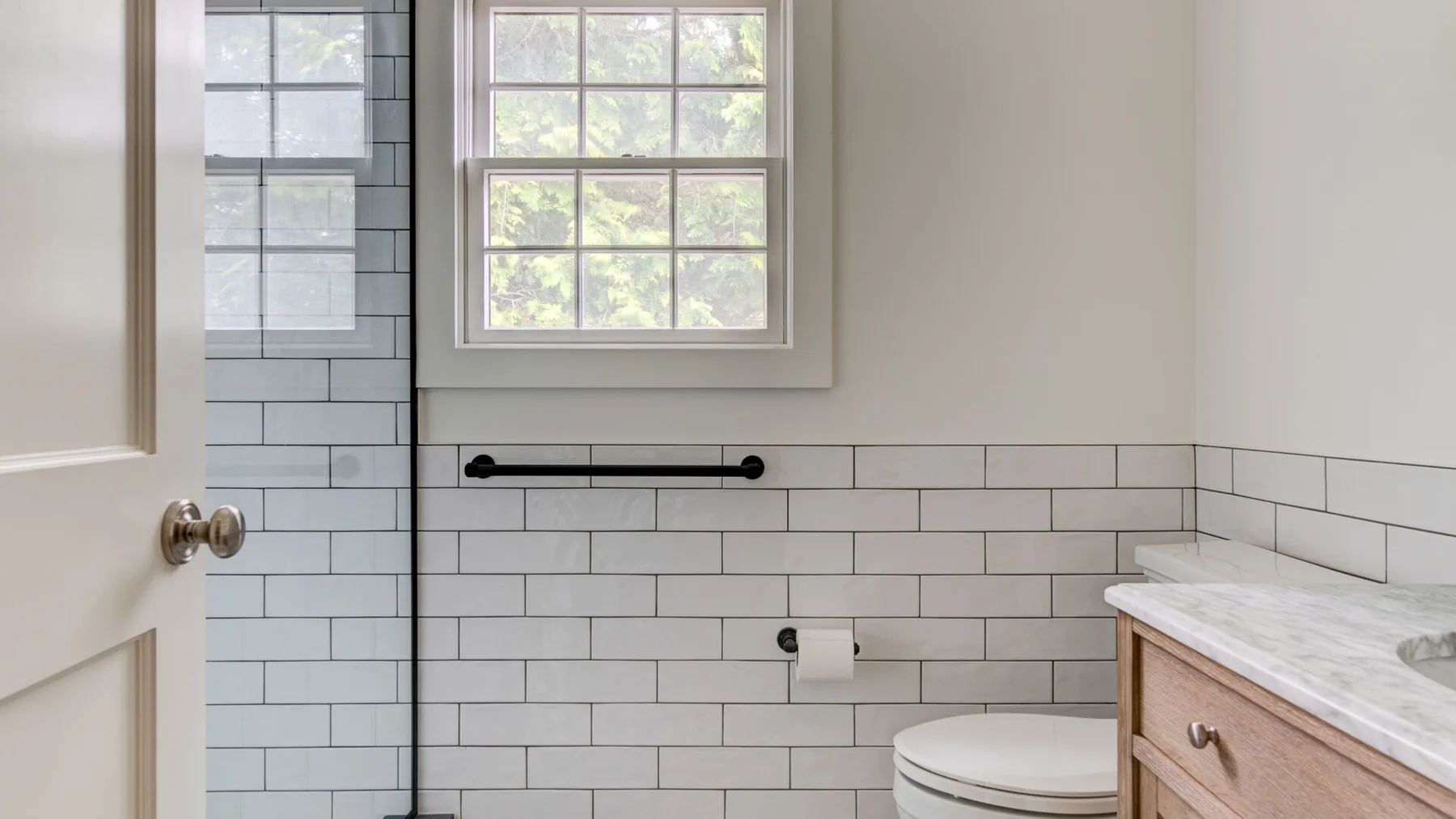 A bright bathroom with white tiled walls, a window, and a vanity.