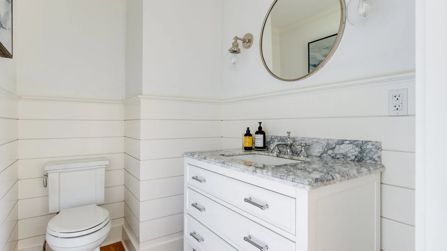 A bathroom vanity with a marble-patterned countertop and a toilet beside it.