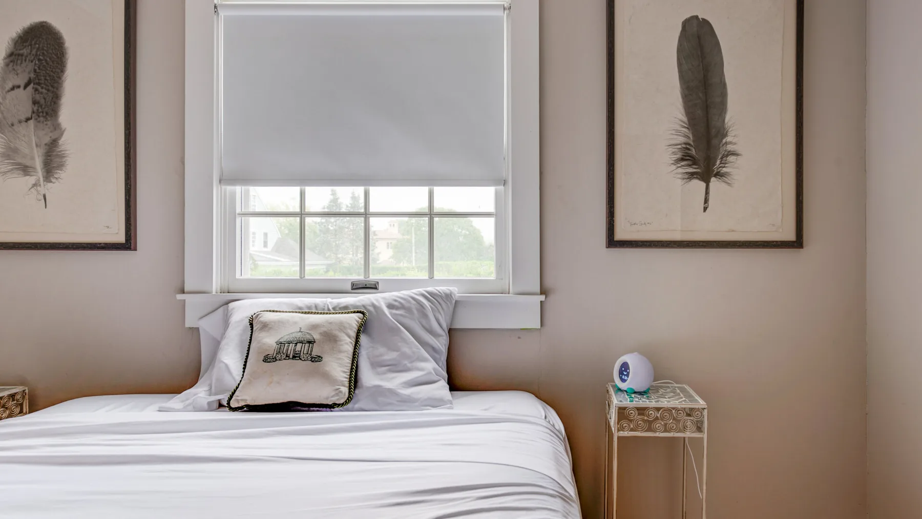 A bedroom with a neatly made bed, feather prints, and a window.