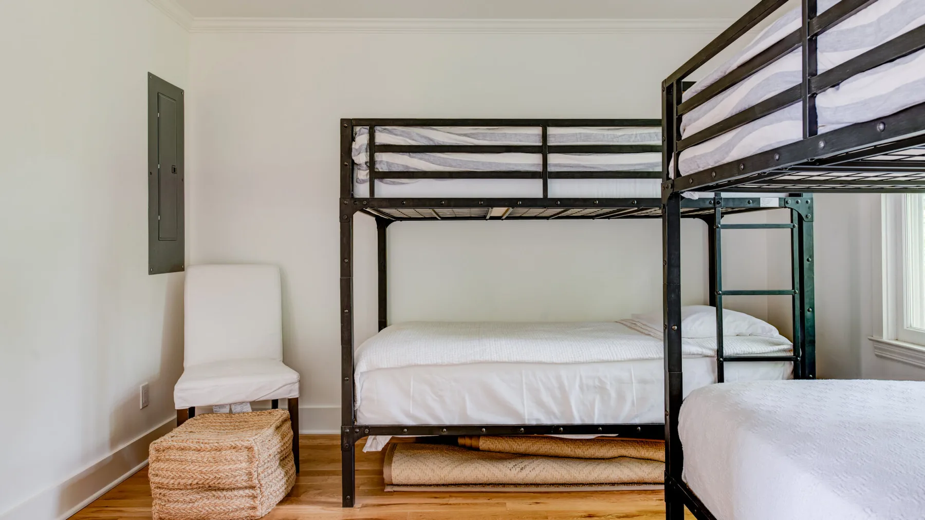 A bunk-bed room with white bedding and woven baskets beside the bed.