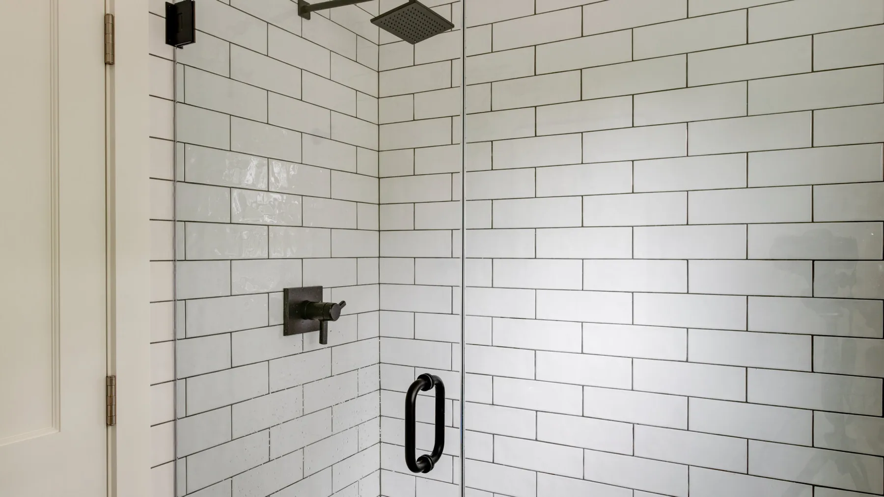 A tiled shower with a dark showerhead and wall-mounted controls.