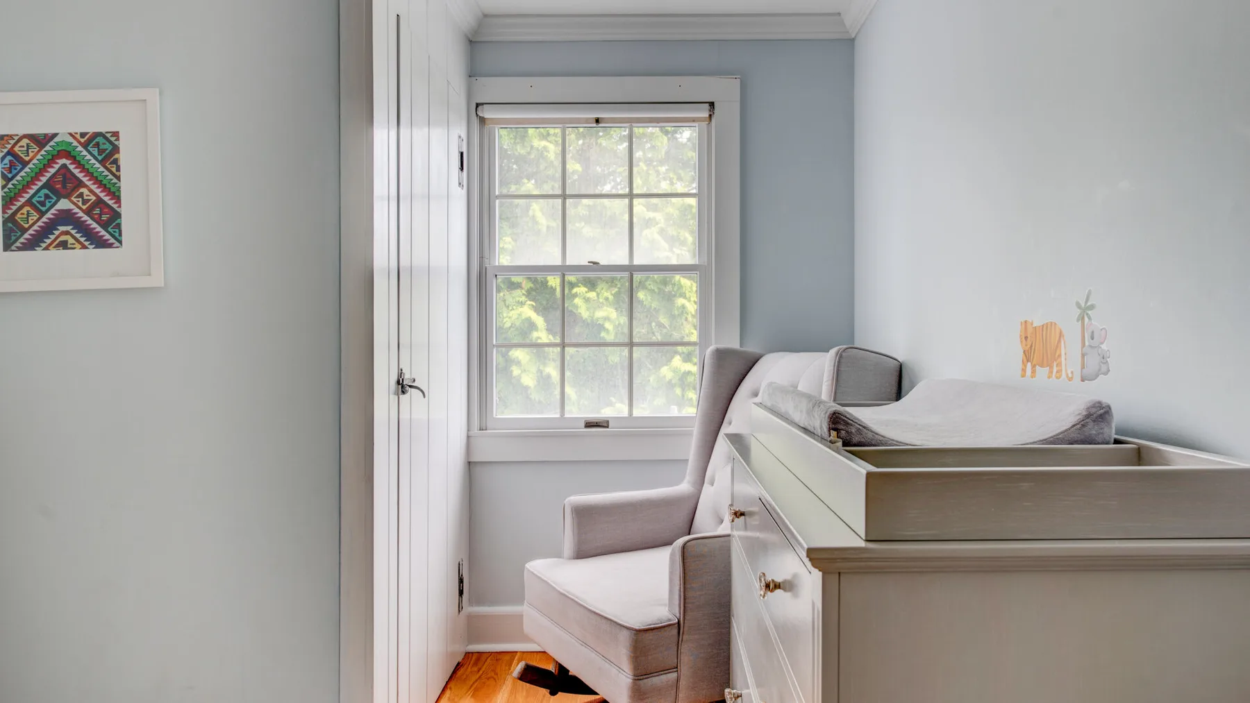 A bright room with a window, an upholstered chair, and a changing table.