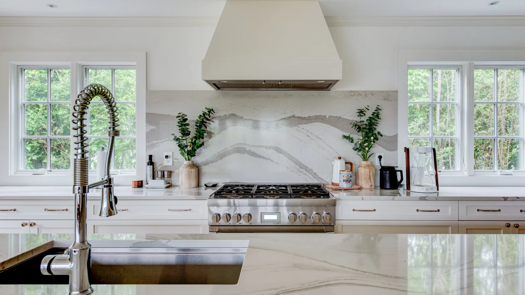 A bright kitchen with white cabinetry, a central range, and large windows.