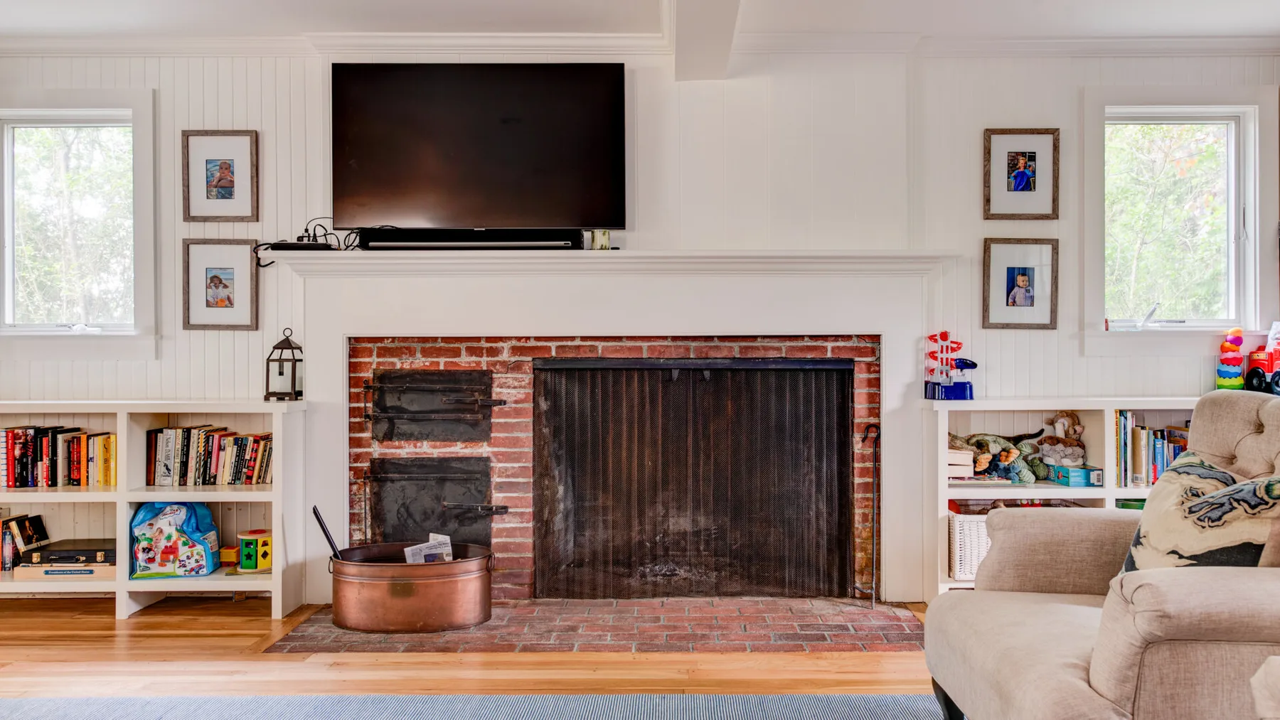 A living room with a brick fireplace, television, and built-in shelves.