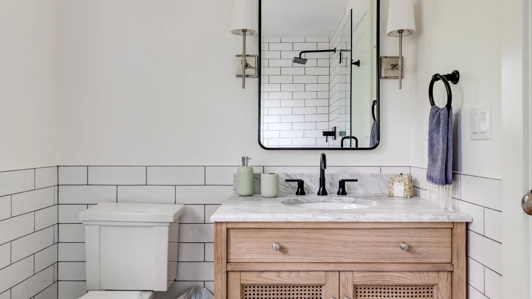 A bright bathroom with a wood vanity, sink, and tiled walls.