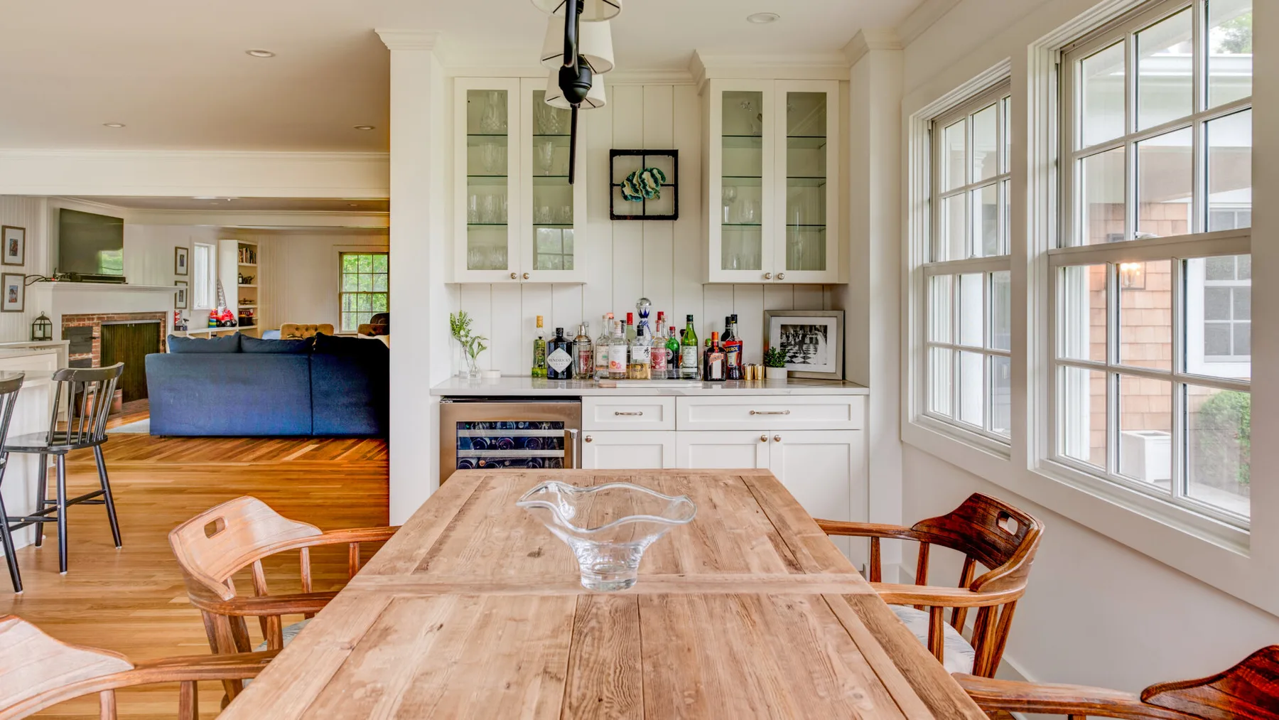 A bright dining area with a long wooden table beside large windows.