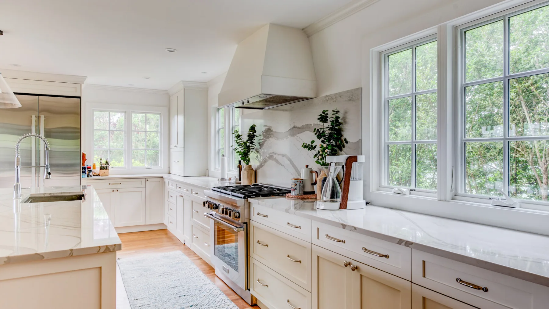A bright kitchen with white cabinetry, a central island, and large windows.