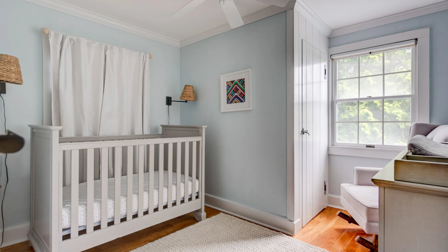 A nursery with a white crib, pale walls, and a window letting in daylight.