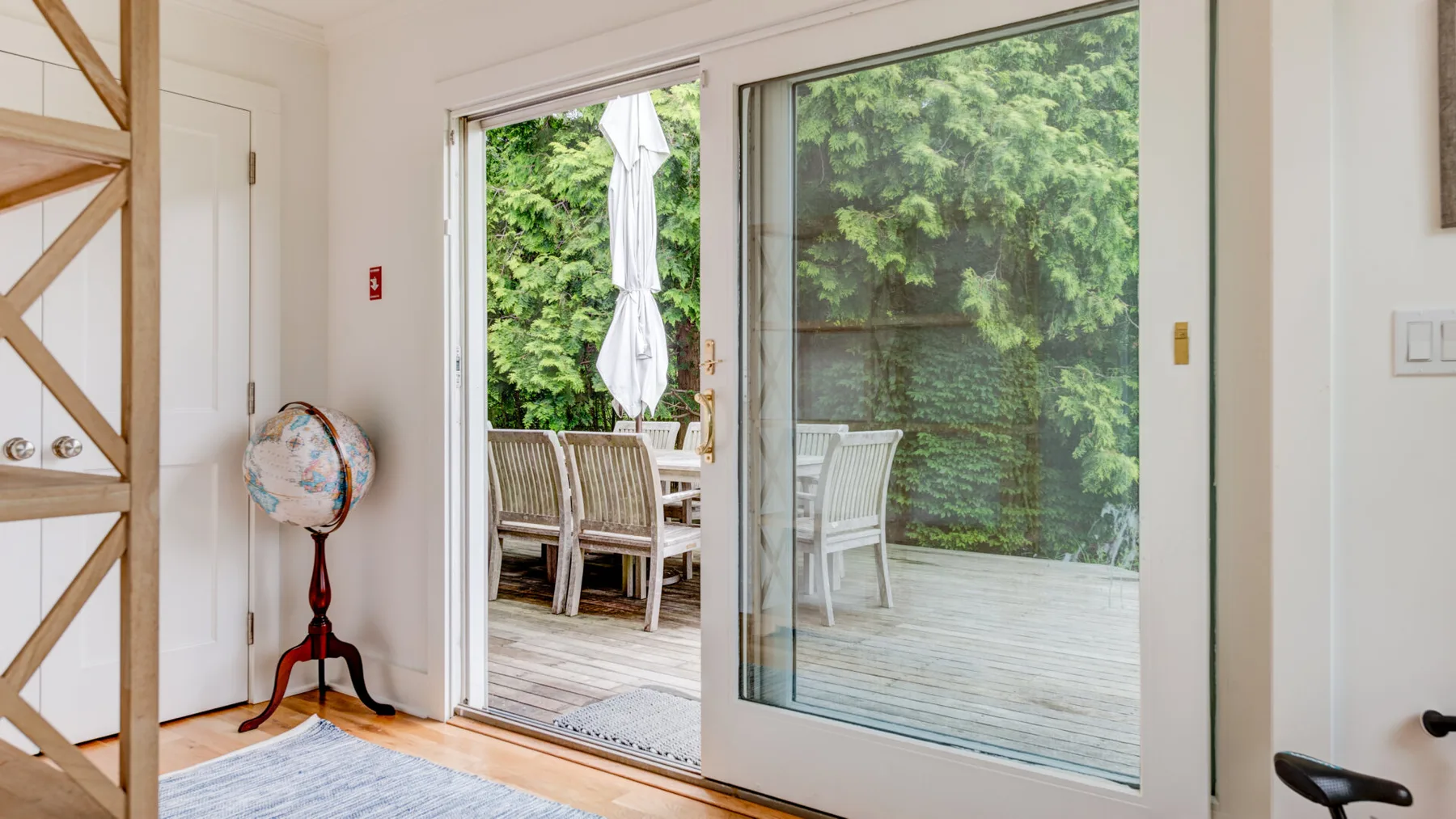 A bright room opens onto a wooden deck with outdoor seating and greenery.