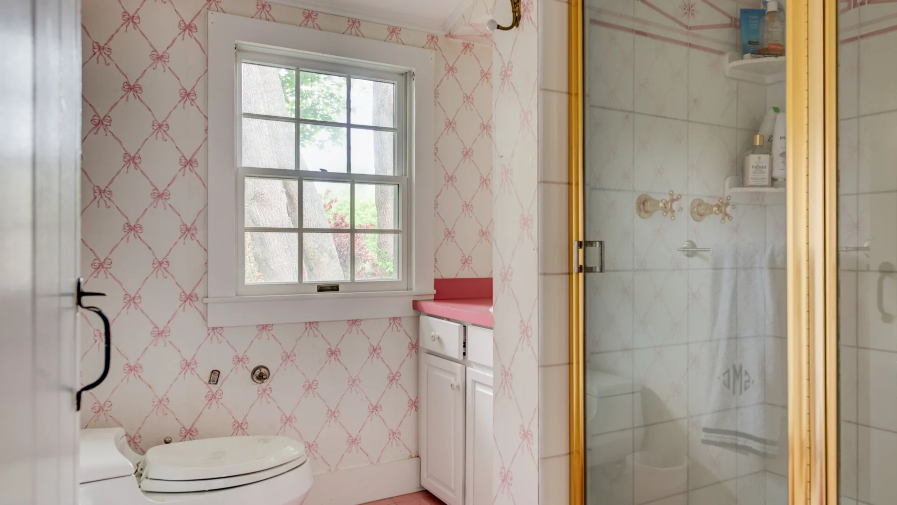 A bathroom with a window, toilet, vanity, and glass shower.