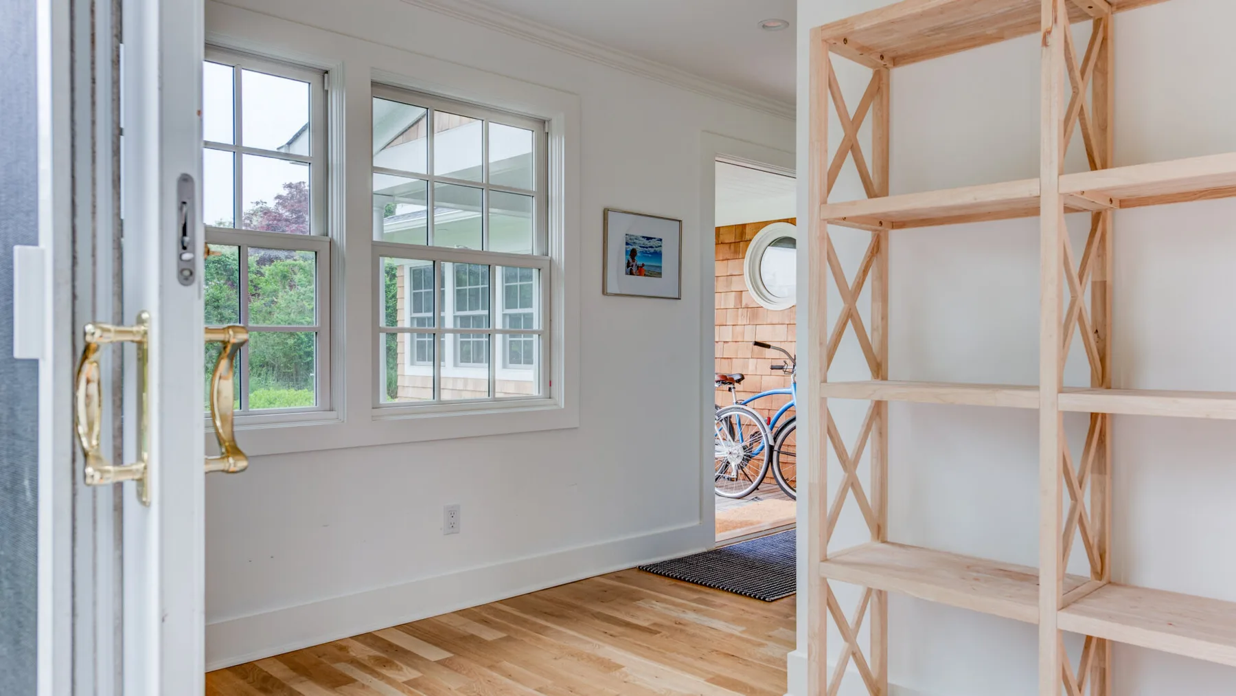A bright room with large windows and an open wooden shelving unit.