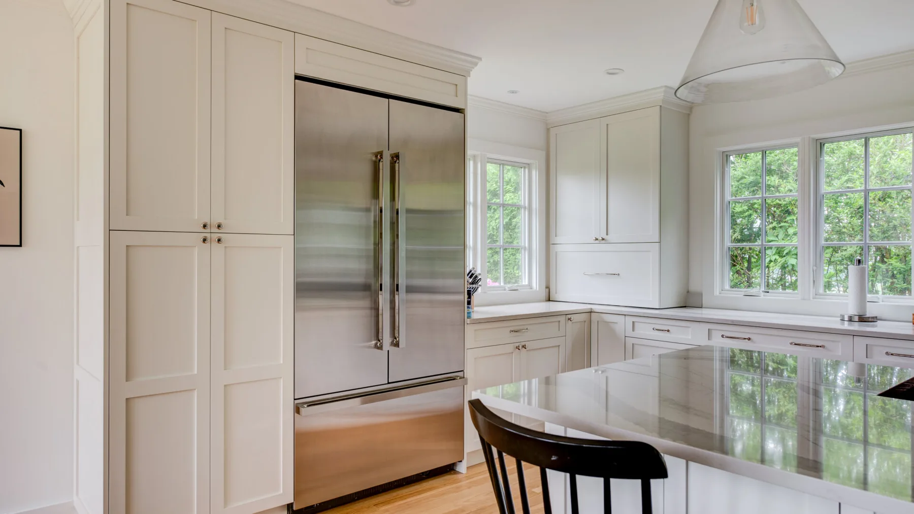 A bright white kitchen features a large island and stainless steel refrigerator.