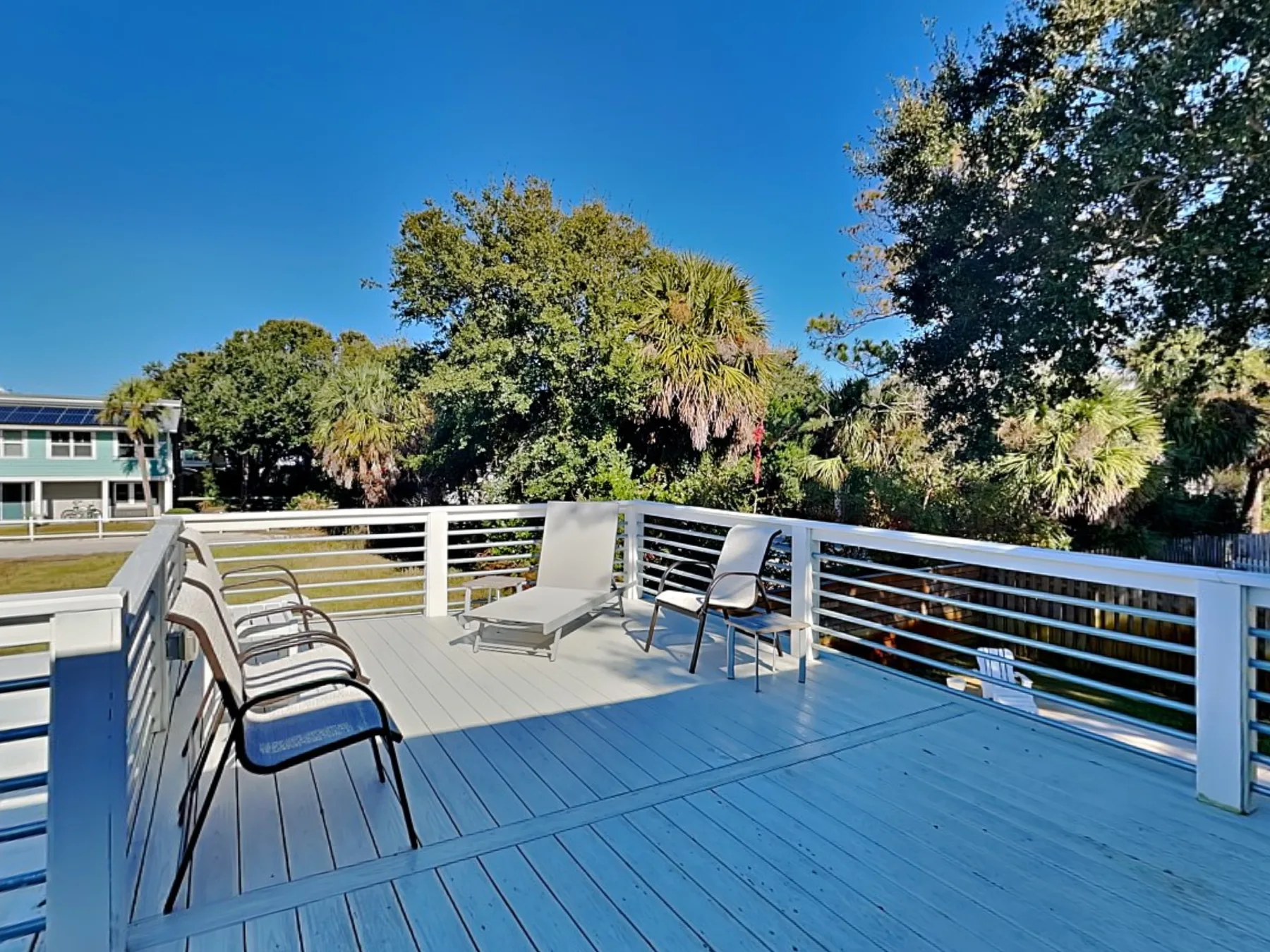 Outdoor deck with seating and white railings overlooks leafy trees.