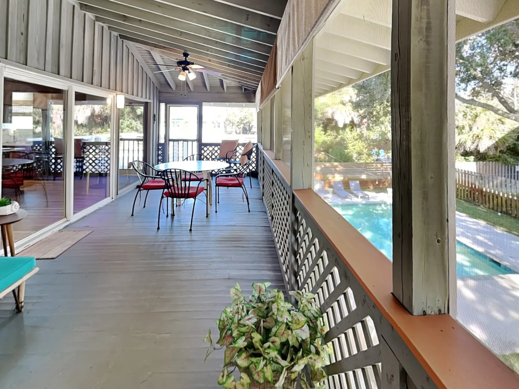 A covered deck with a dining table overlooks a swimming pool.
