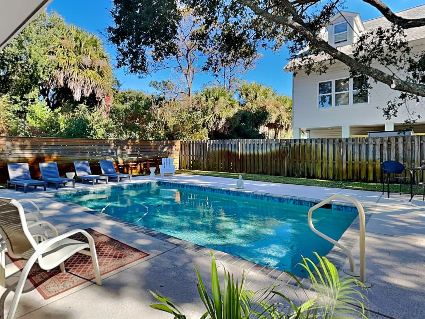 An outdoor swimming pool is surrounded by deck seating and leafy trees.