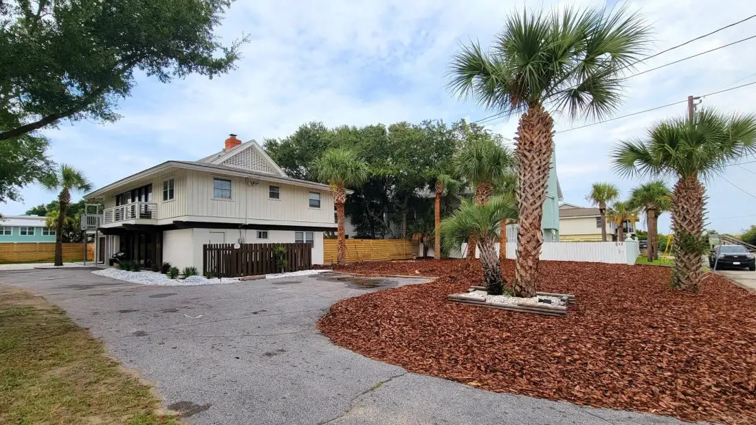 A low-rise building stands beside a paved parking area and palm trees.