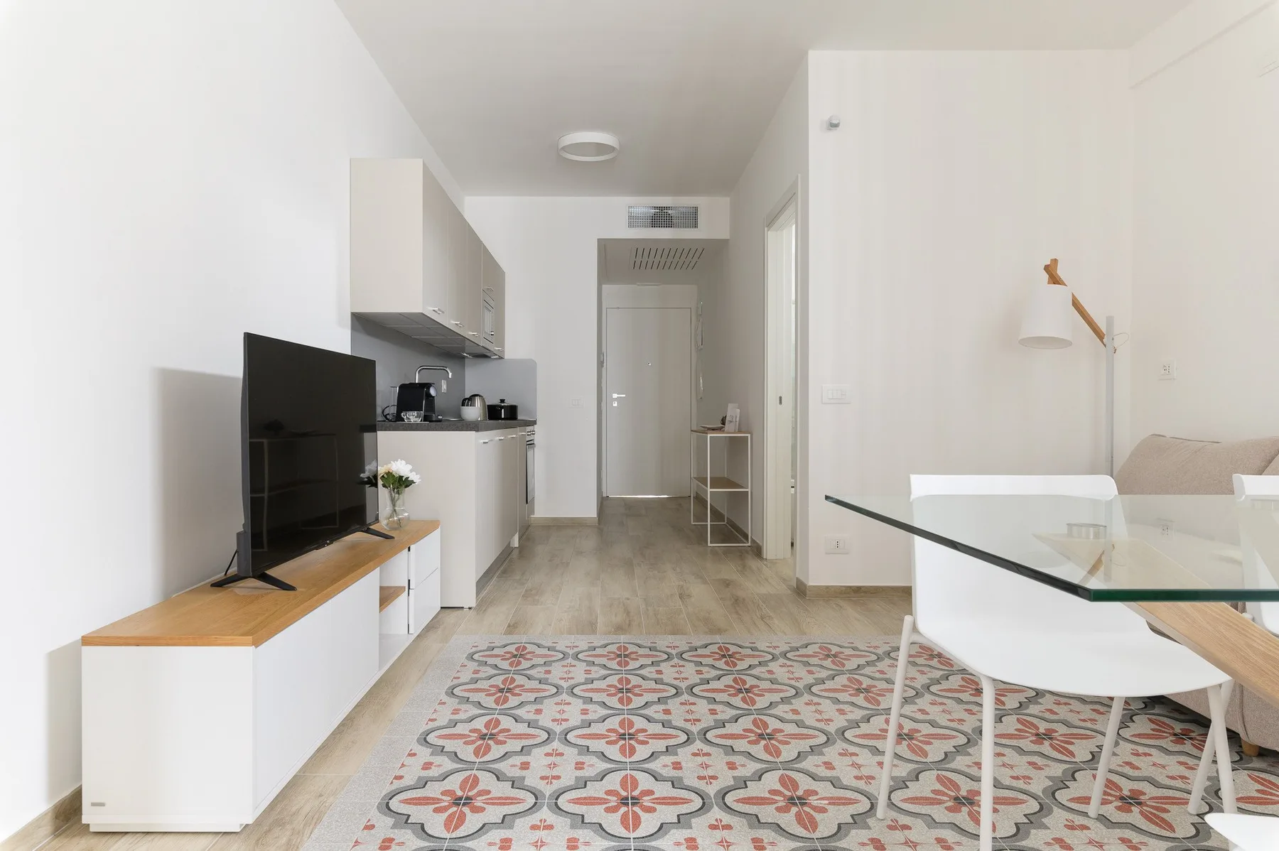 A bright living area with a compact kitchen, dining table, and patterned rug.