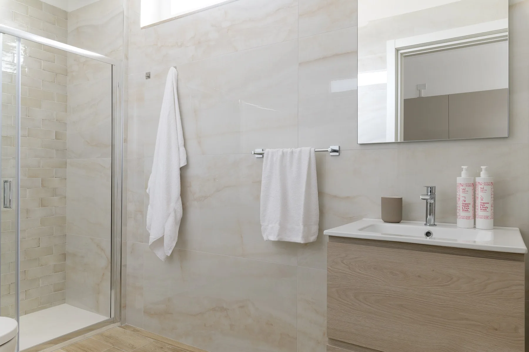 A bright bathroom with a glass shower, sink, and white towels.