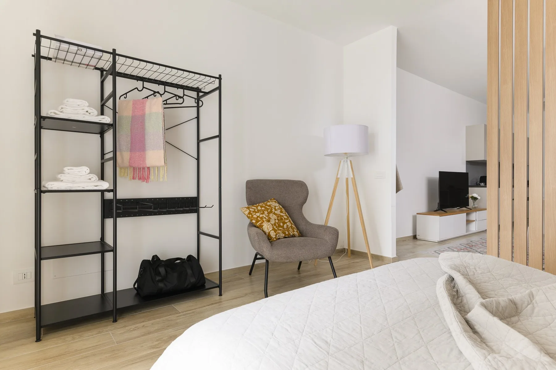 A bright bedroom with a bed, an armchair, and an open clothes rack.