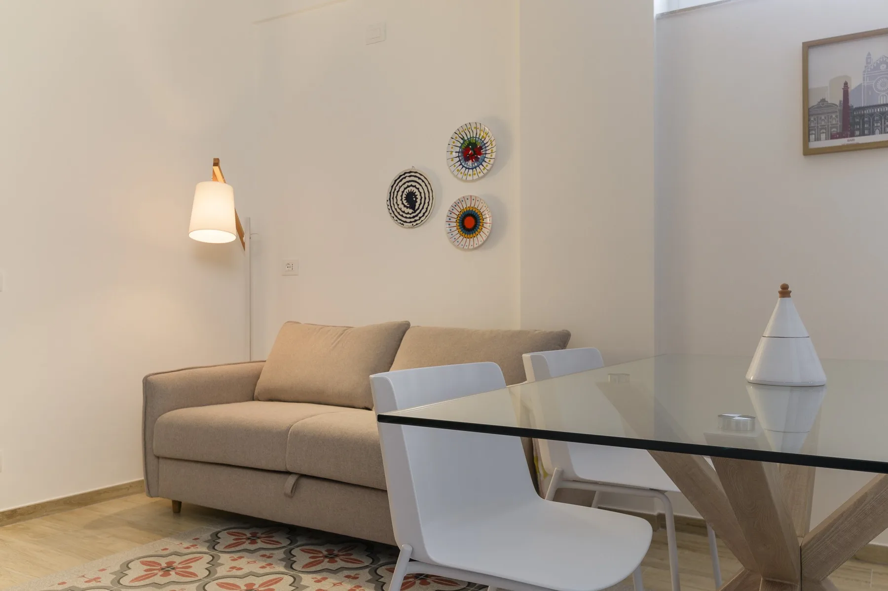 A living and dining area with a sofa, glass table, and decorative wall art.