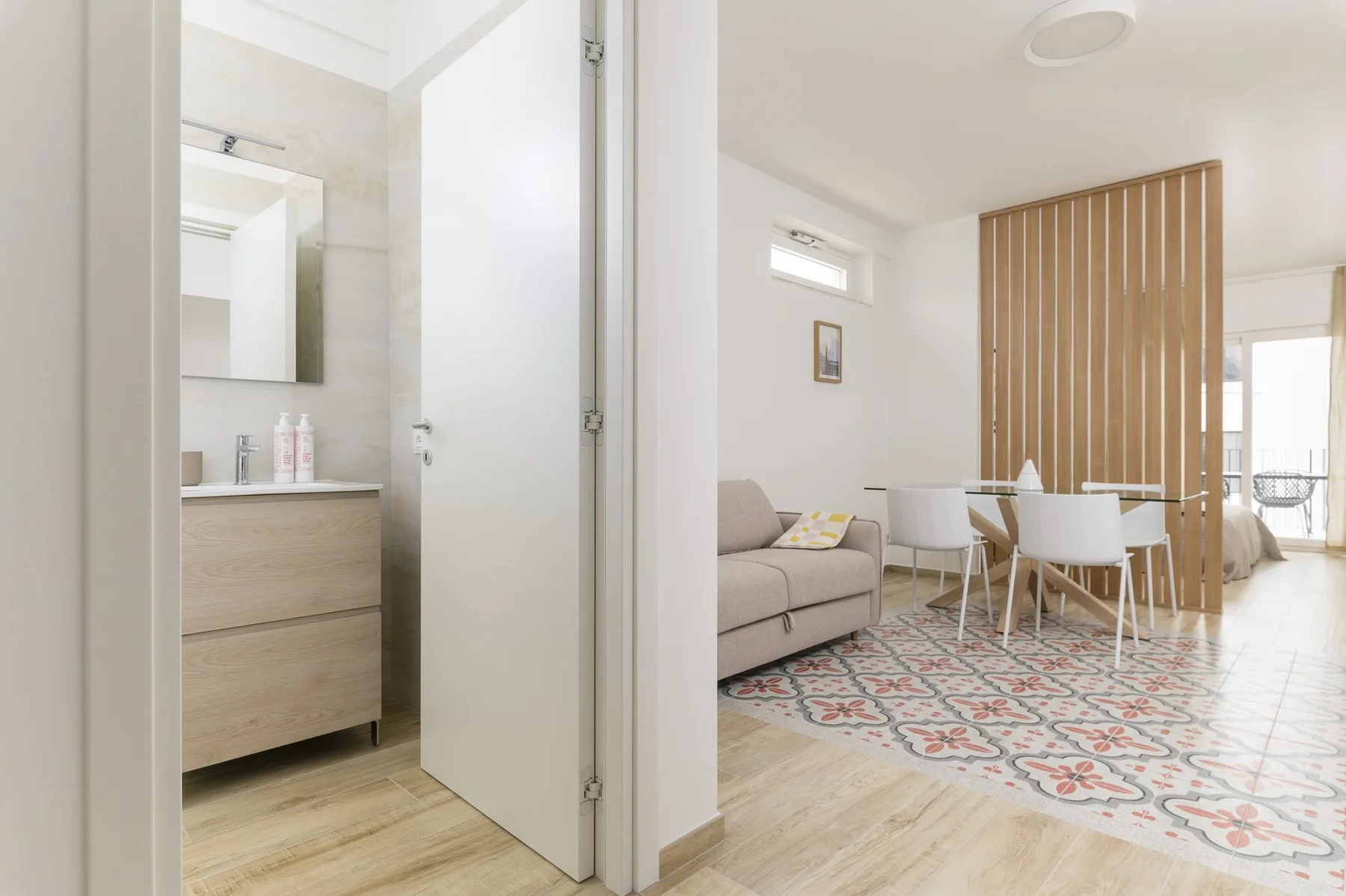 A bathroom opens onto a bright living and dining area with a patterned rug.