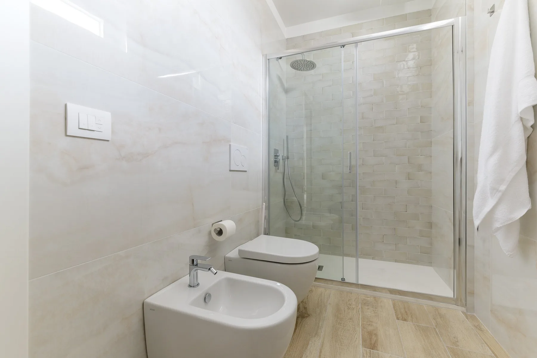 A bright bathroom with a glass shower and white bathroom fixtures.