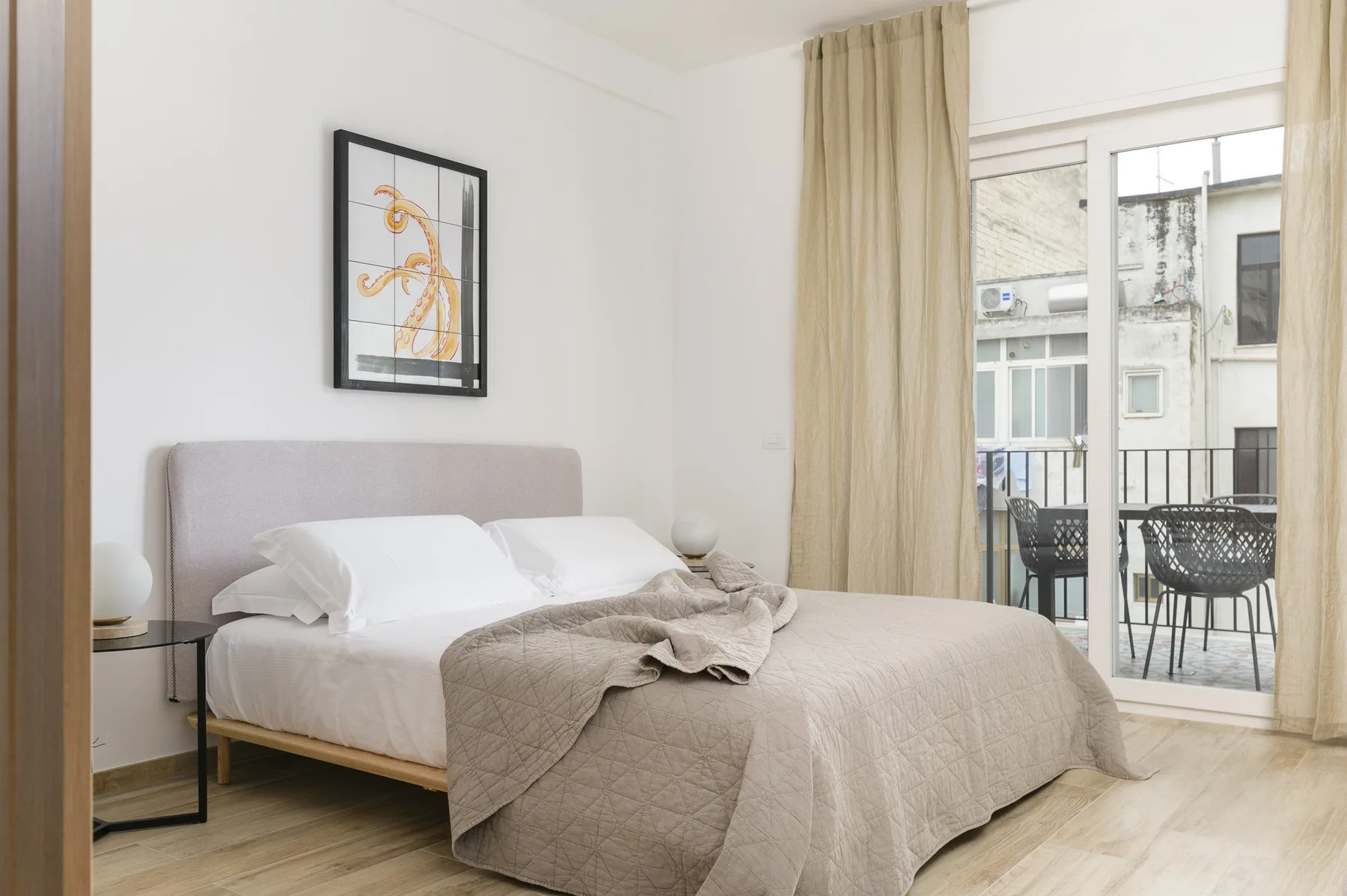 A bright bedroom with a neatly made bed and glass doors opening onto a balcony.