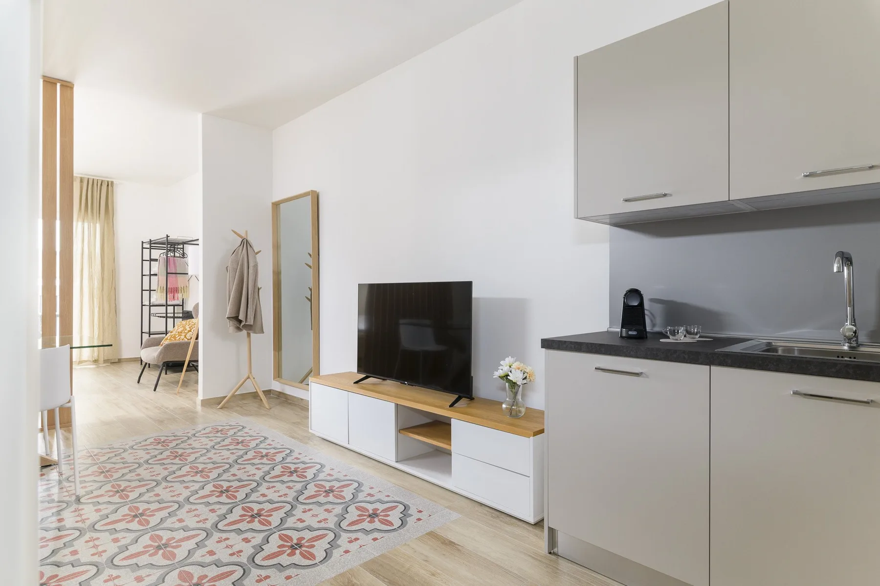 A bright living area with a television, seating, and an open kitchenette.