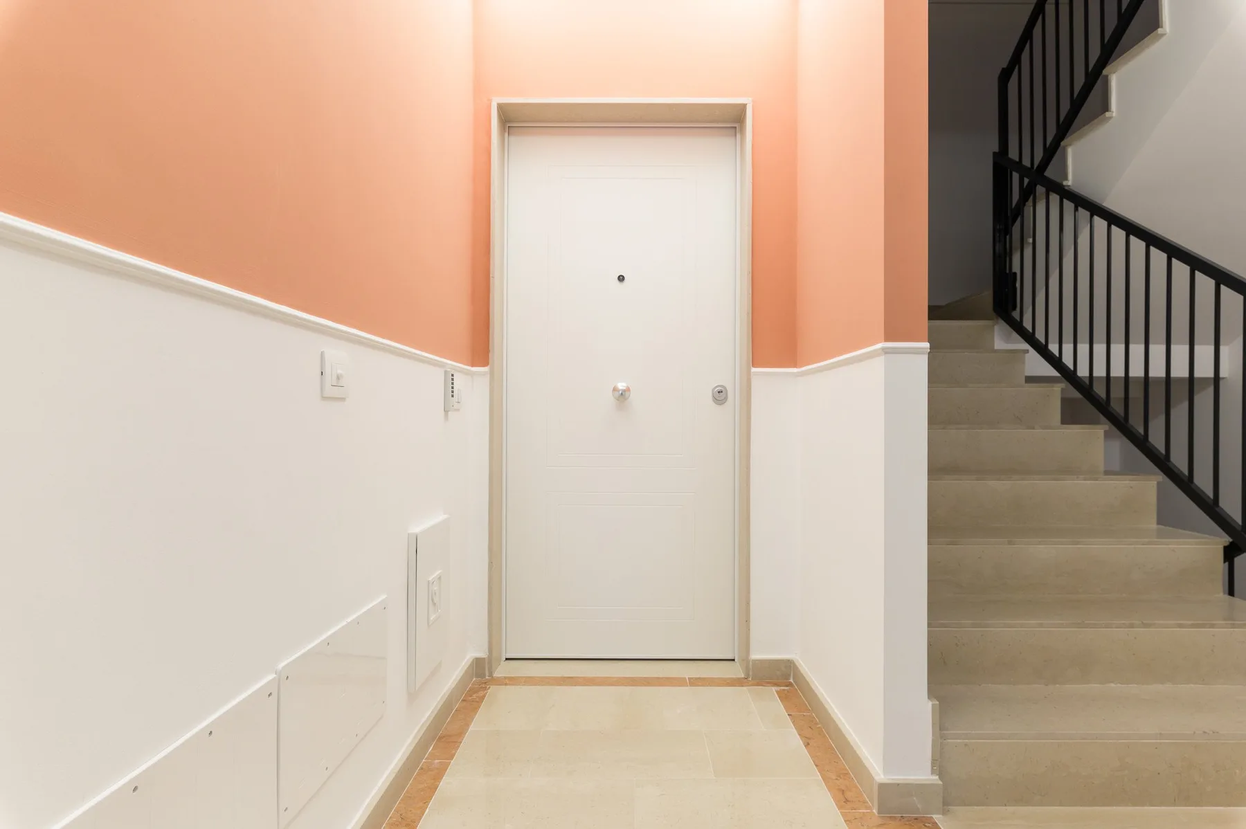 A hallway with a white door and a staircase with dark railings.