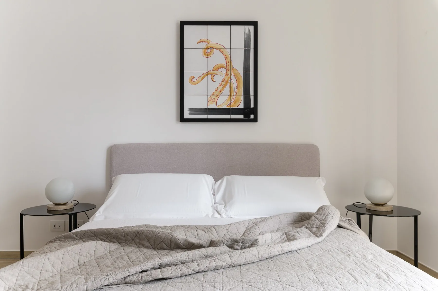 A bedroom with a double bed, white pillows, and framed artwork above the headboard.