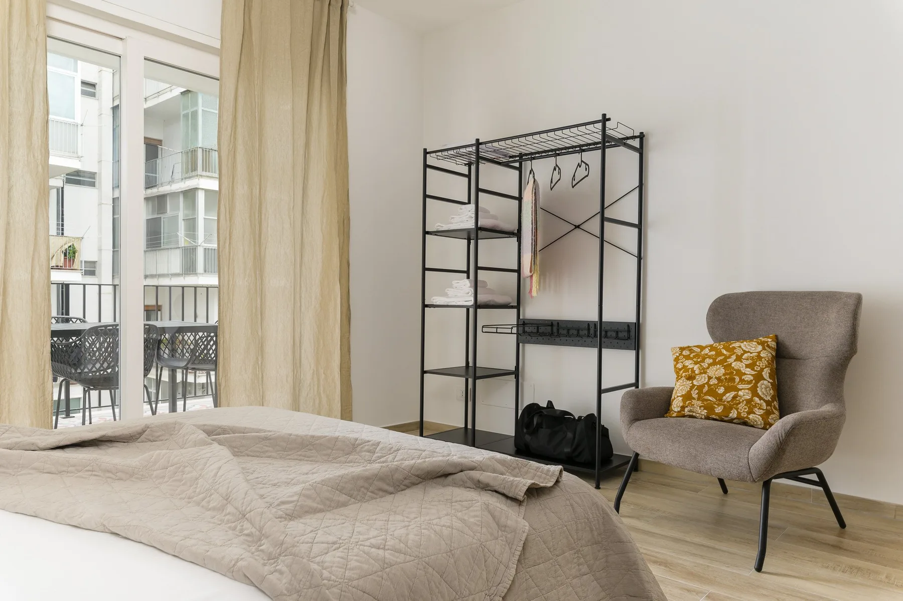 A bedroom with a bed, an open clothing rack, and an upholstered chair.