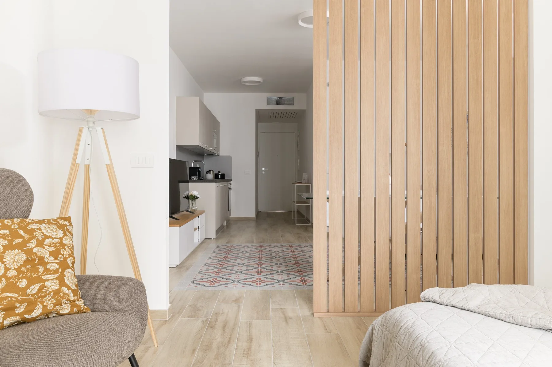 A bright living area opens onto a compact kitchen, with a wooden slat divider beside the bed.