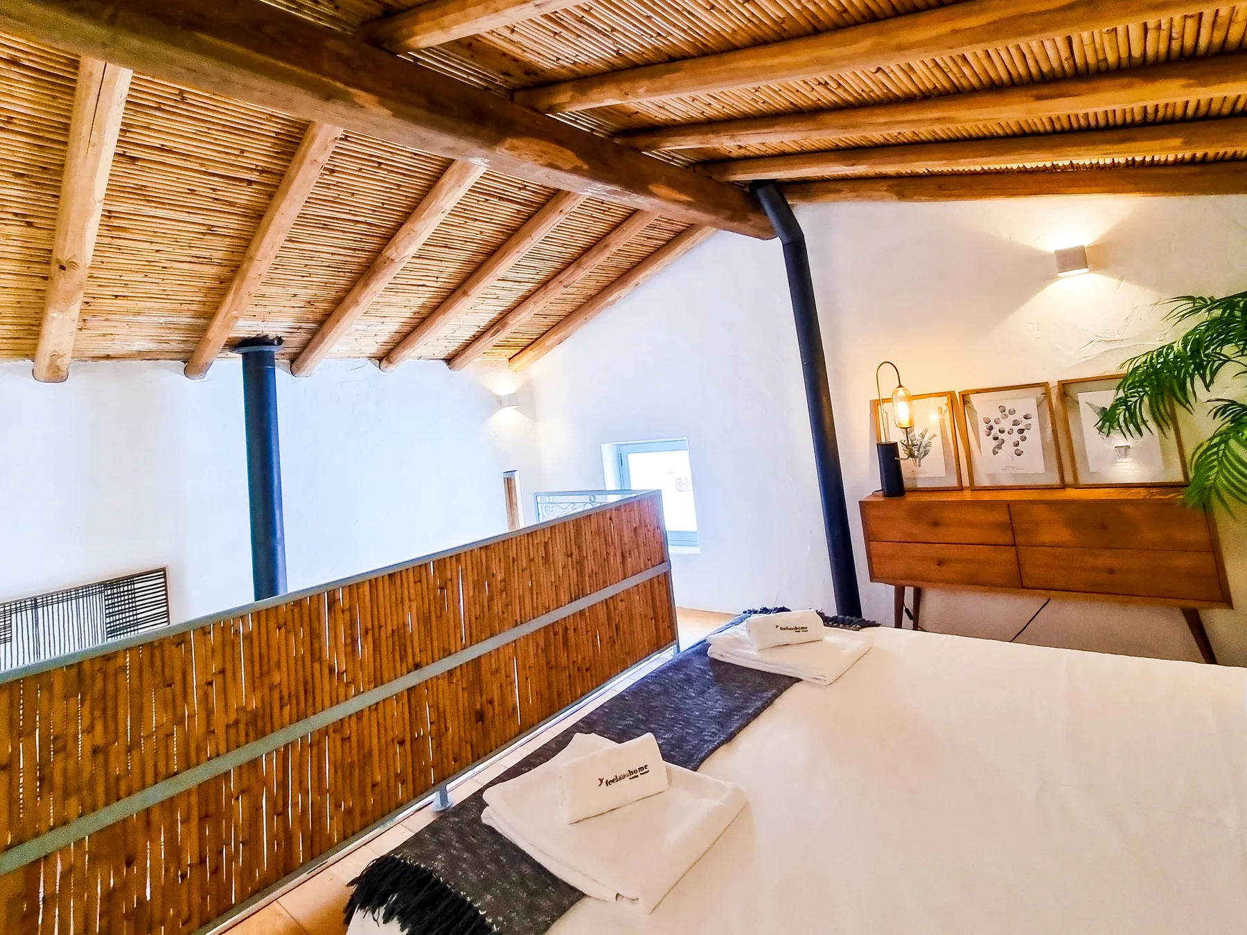 Un dormitorio con una cama baja junto a una barandilla de bambú y un techo inclinado de madera.