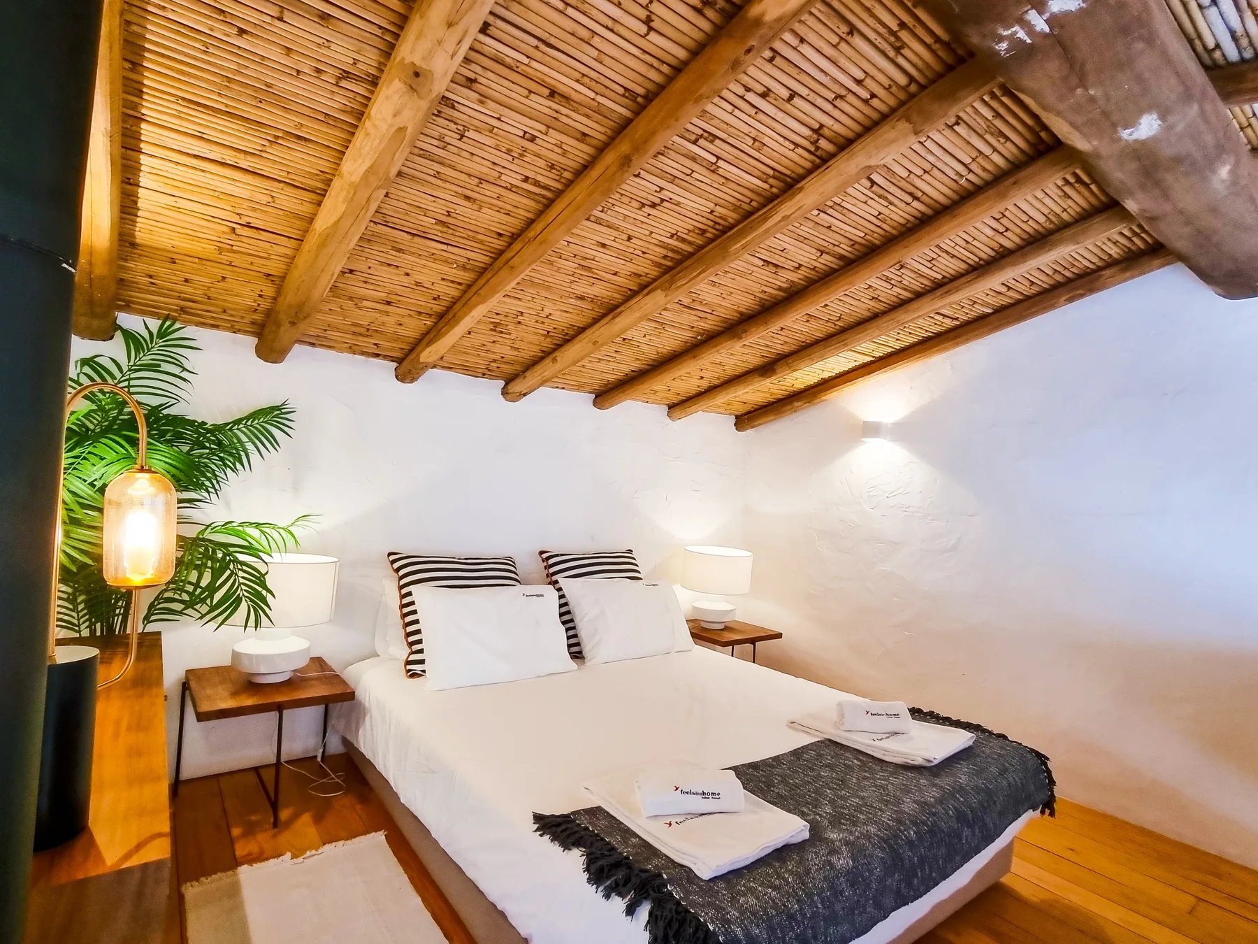 Un dormitorio con una cama bajo un techo inclinado de madera y mesitas de noche.