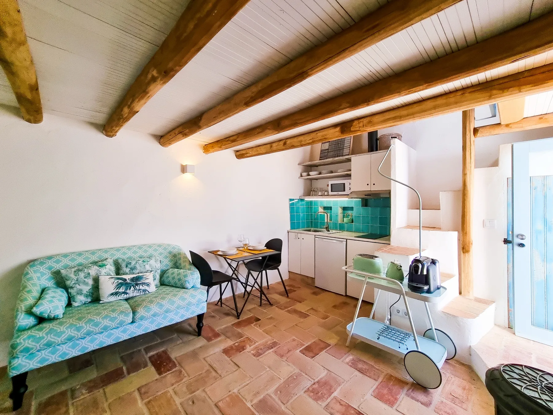 Una pequeña sala de estar con asientos estampados, una mesa de comedor y una cocina.