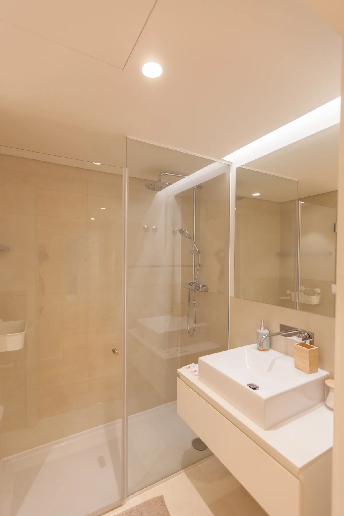 Un baño con azulejos beige, ducha de cristal y lavabo blanco.