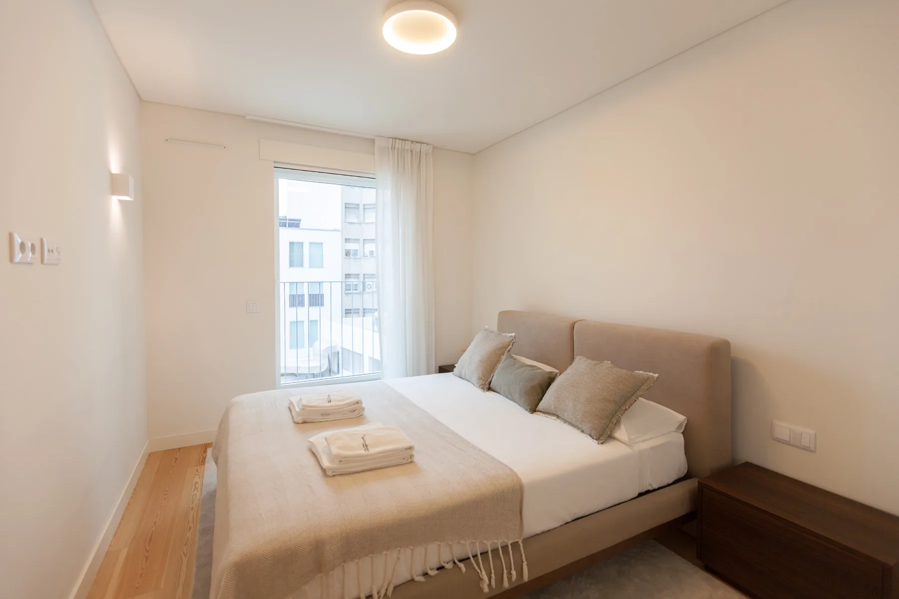 Un dormitorio con una cama y una ventana con vistas a edificios cercanos.