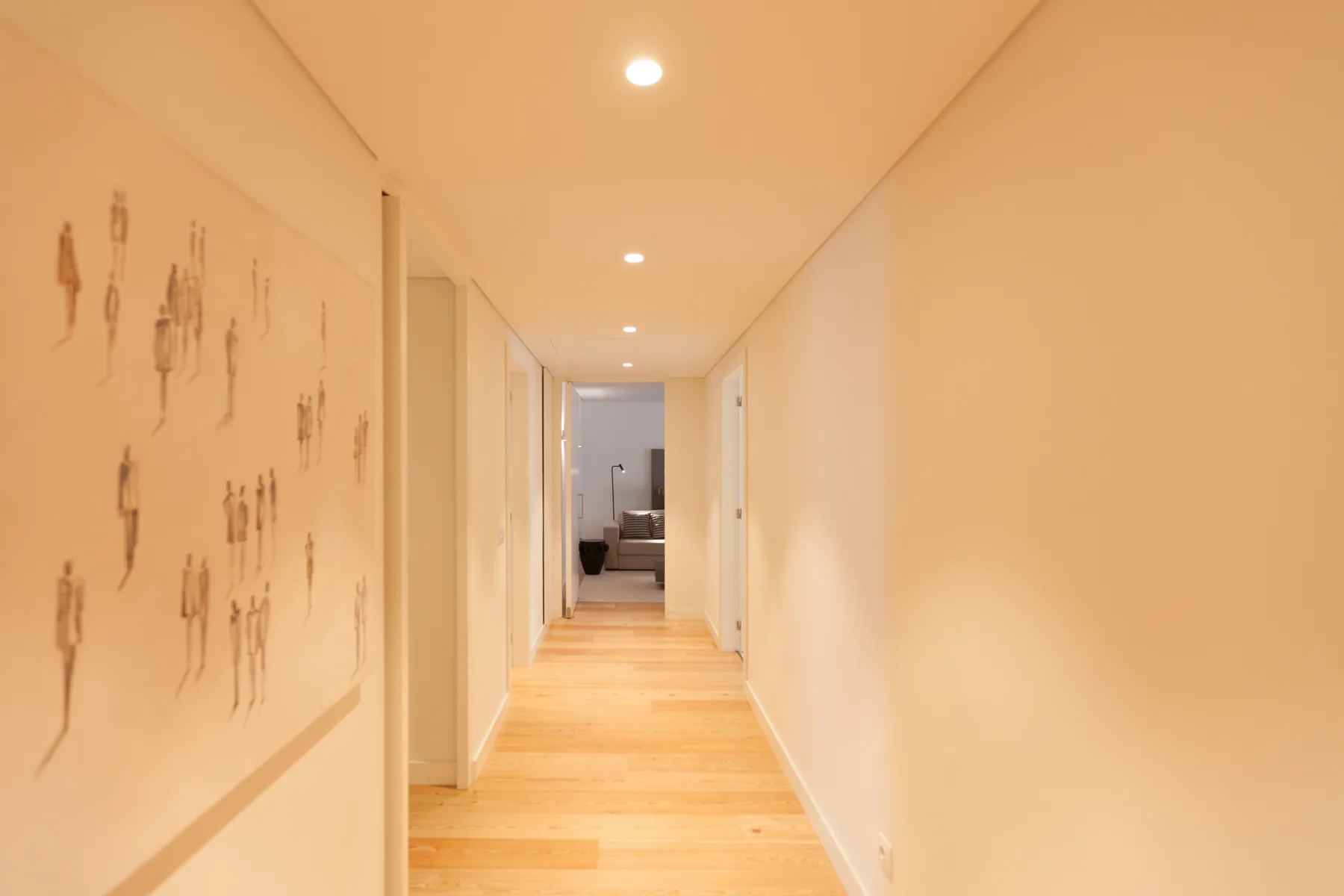 Un pasillo luminoso con suelo de madera clara y obras enmarcadas.