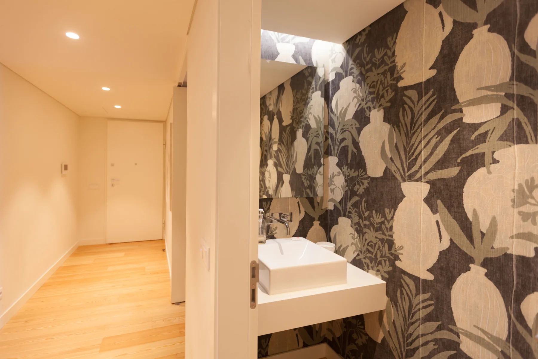Un lavabo de baño con una pileta cuadrada está junto a un papel tapiz botánico llamativo.