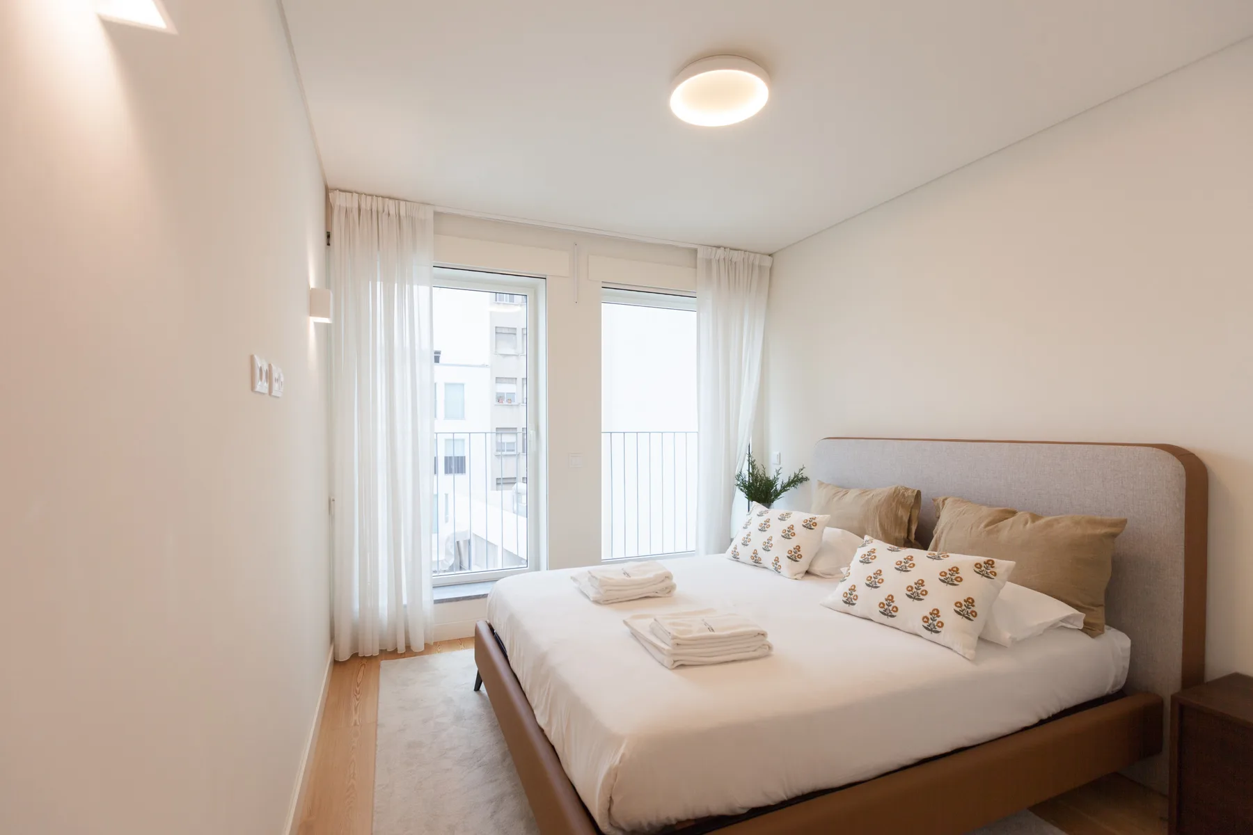 Un dormitorio luminoso con una cama tendida y ventanas altas.