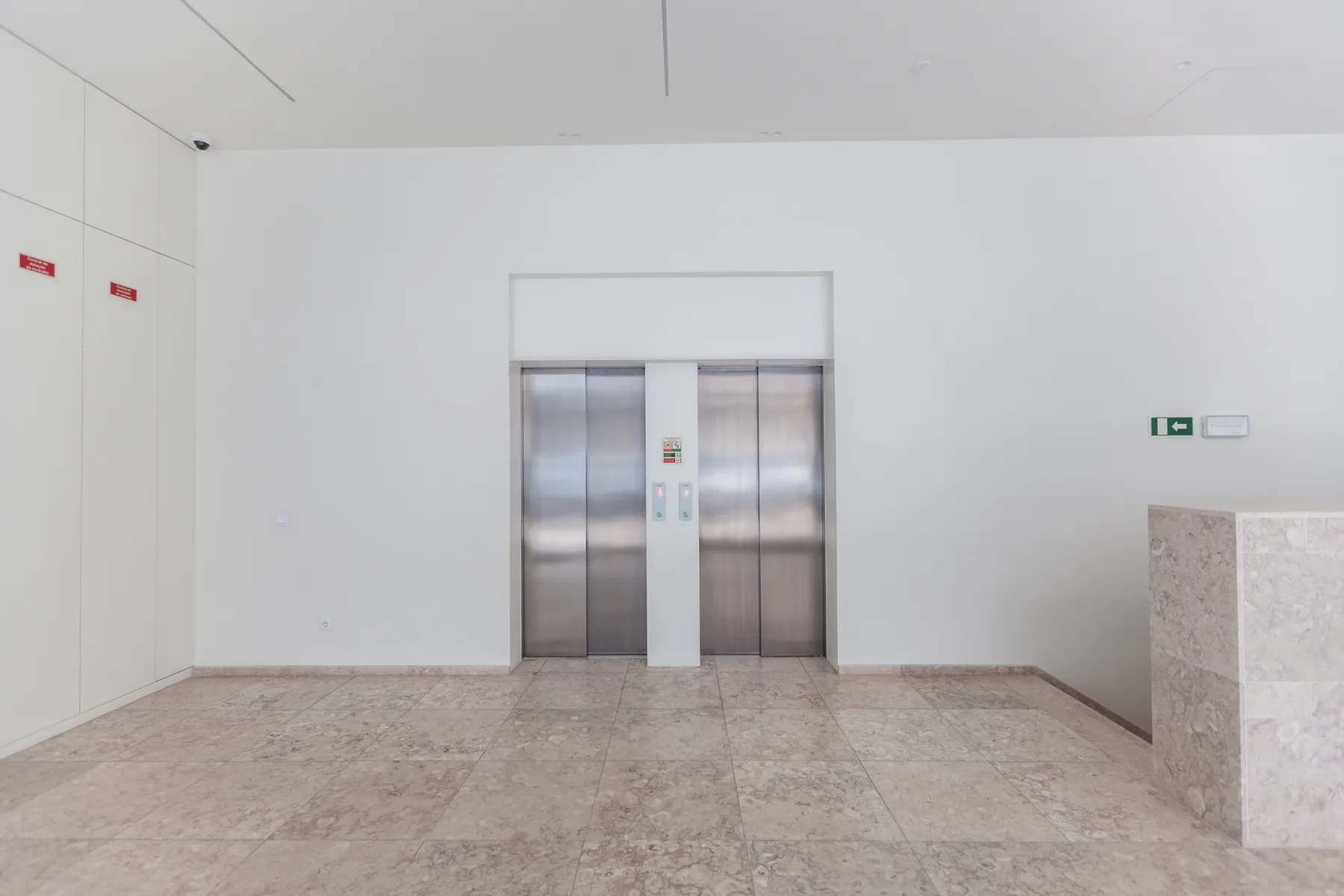 Un vestíbulo luminoso con puertas de ascensor y un mostrador de piedra.