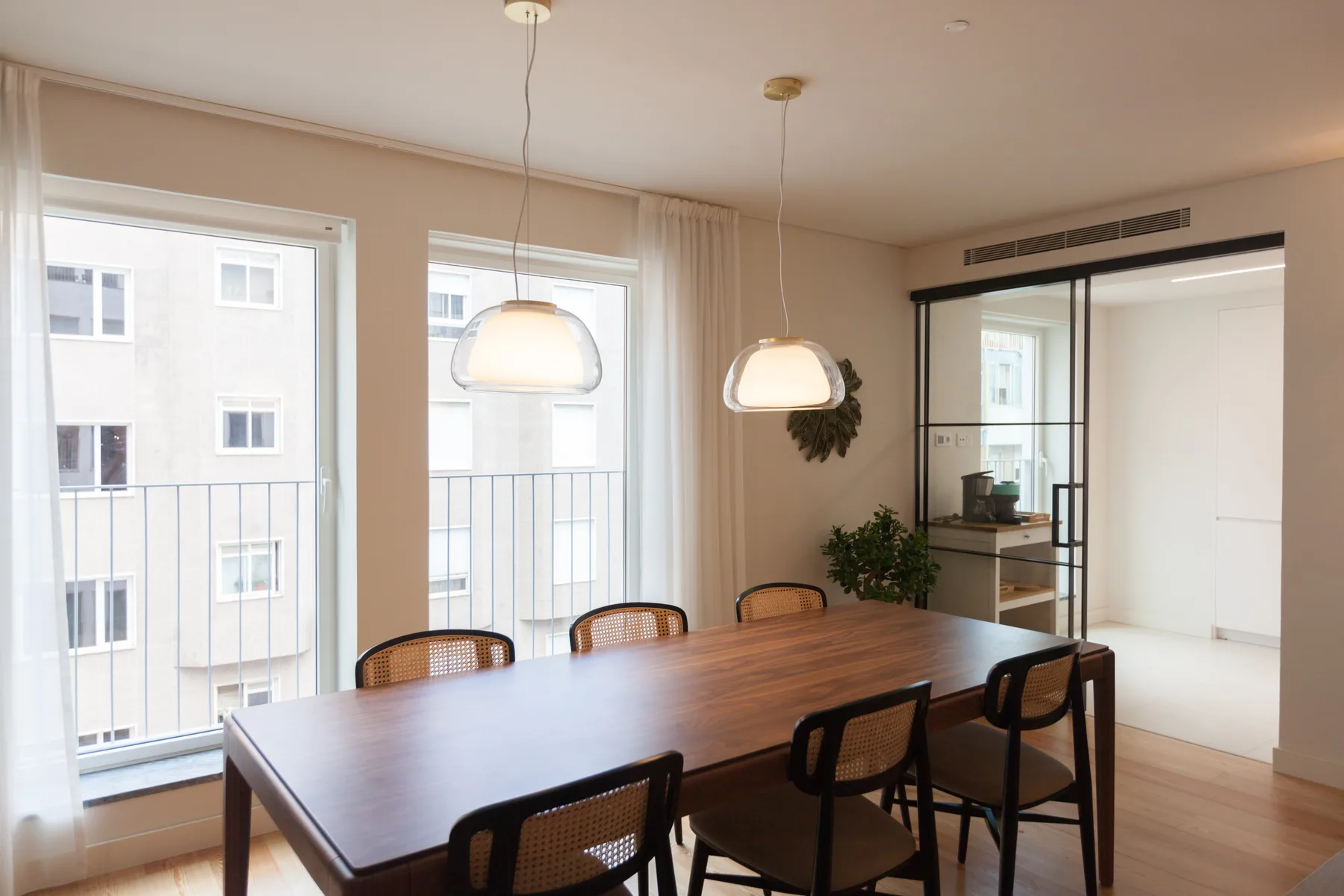 Comedor con una mesa de madera y lámparas colgantes junto a grandes ventanas.