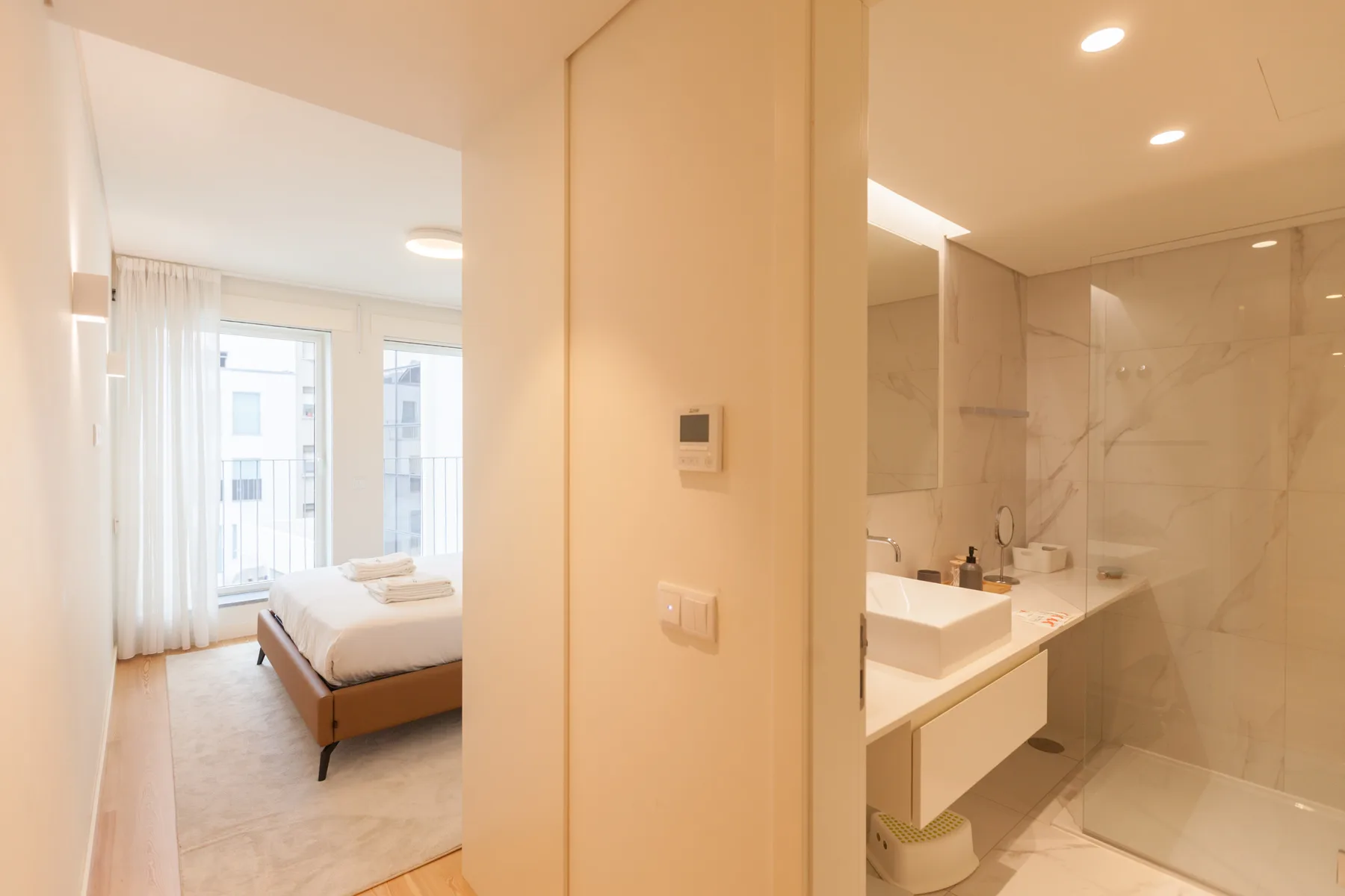 Se ven un dormitorio y un baño contiguo, con una cama y un lavabo.