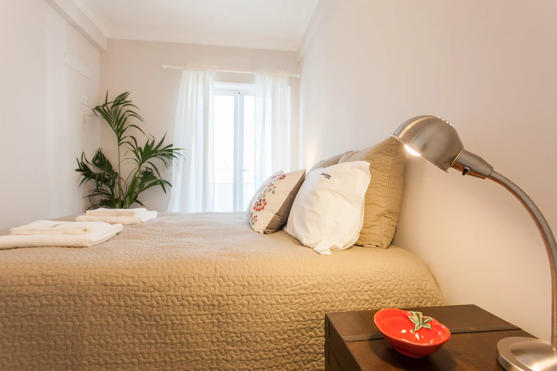 A bright bedroom with a neatly made bed and a potted plant.