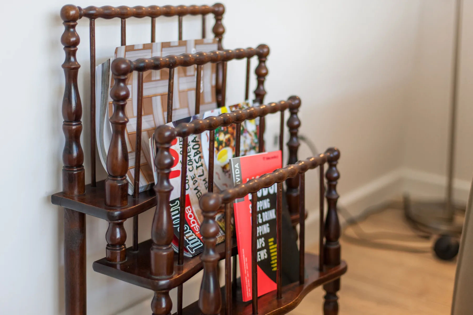 A wooden magazine rack holds books beside a chair in an indoor room.