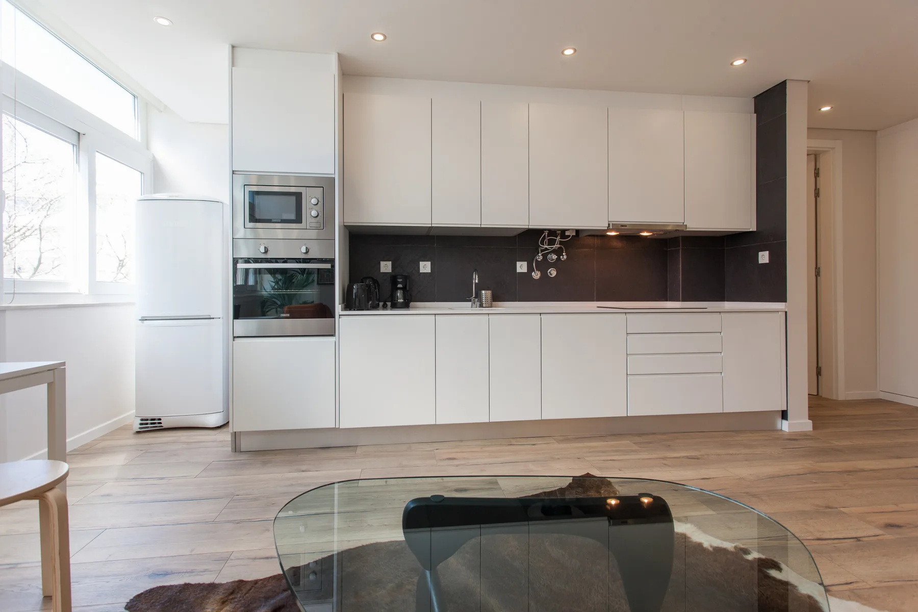 A bright open-plan kitchen and living area with white cabinets and a glass coffee table.