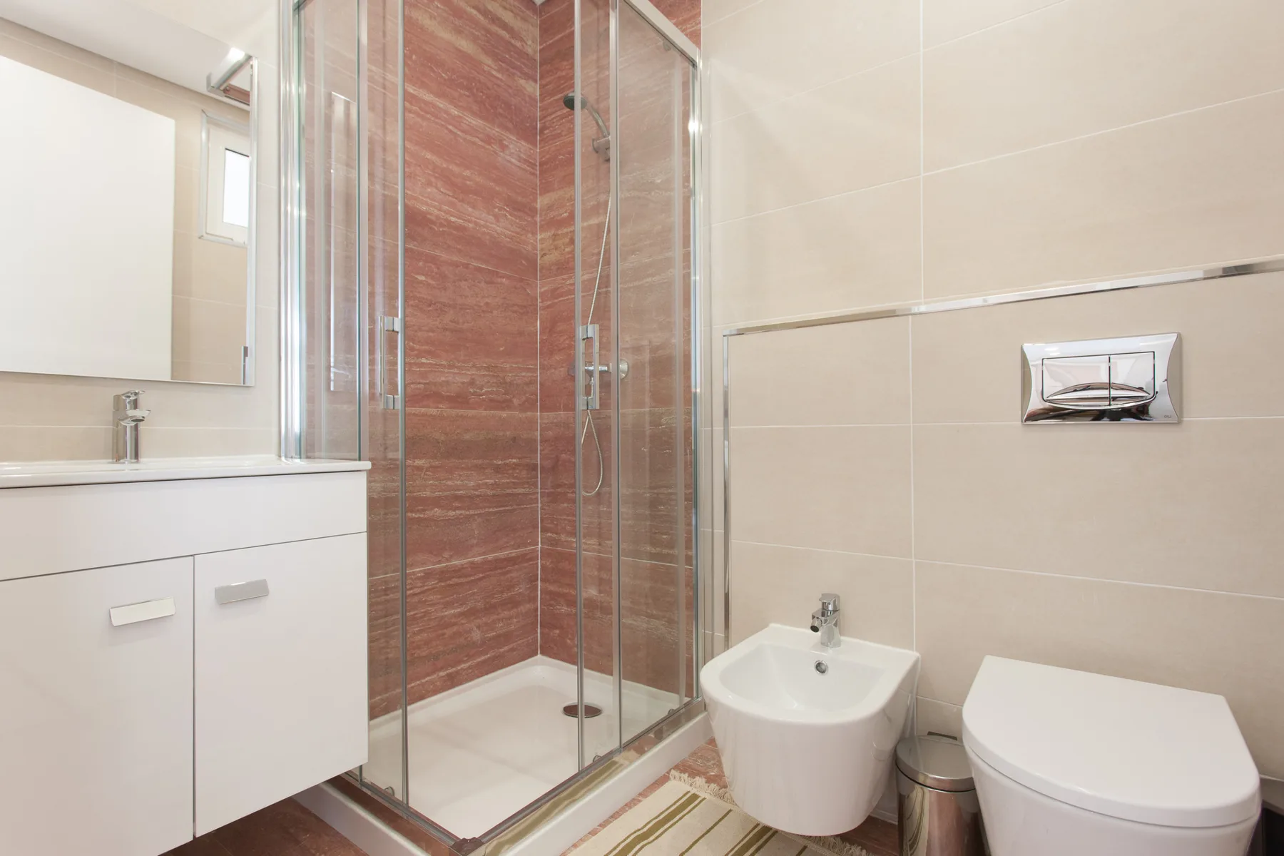 A bright bathroom with a glass shower, sink, and toilet.