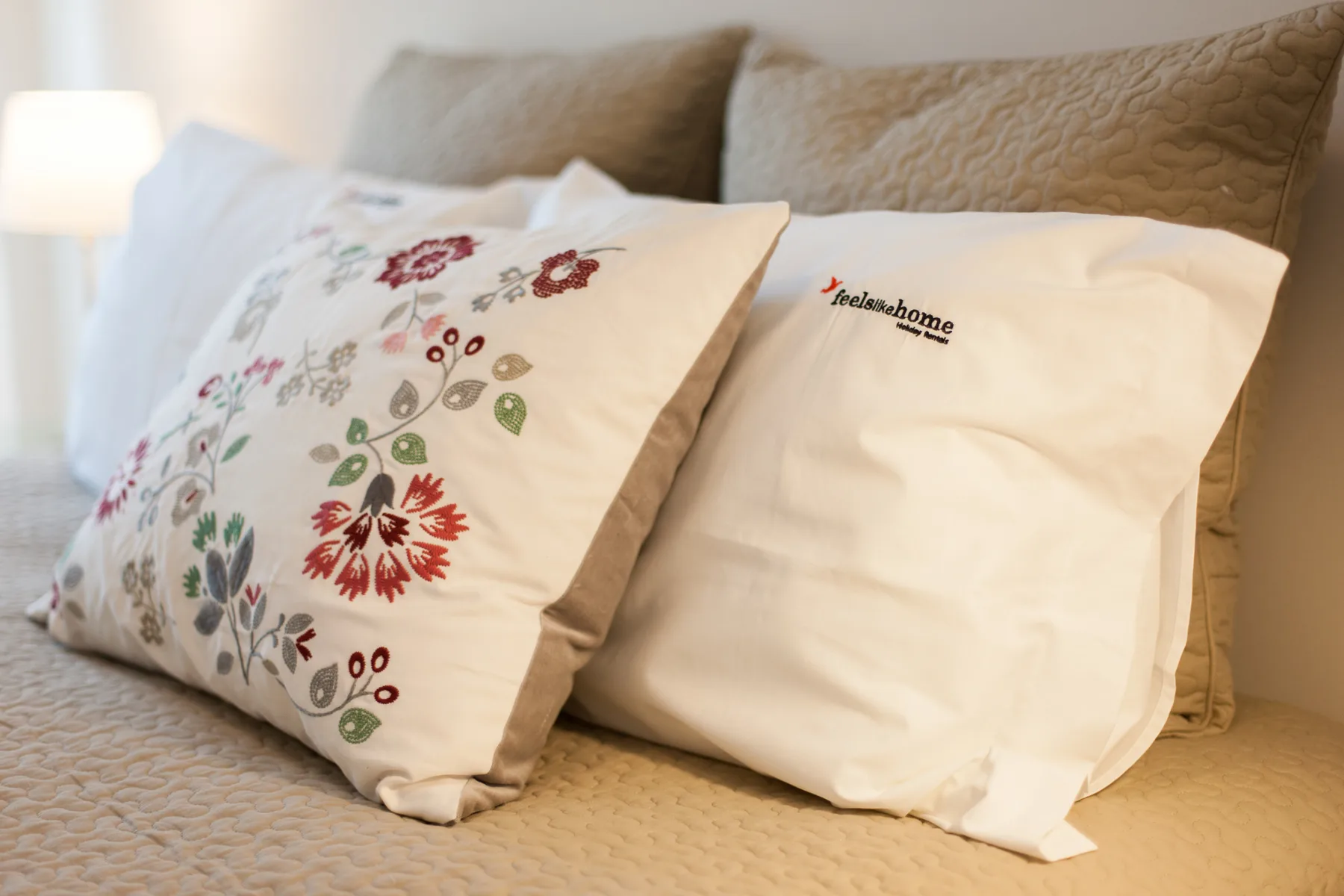 A bed with embroidered decorative pillows and a softly glowing bedside lamp.